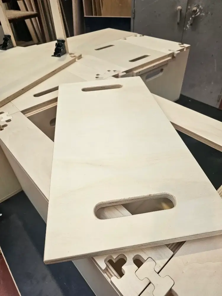 Modules de kit d'aménagement amovible pour van, présentés sur un établi dans un atelier, avec un menuisier en arrière-plan.